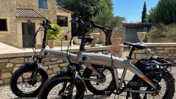 Two bicycles parked in front of a stone building with a tiled roof.