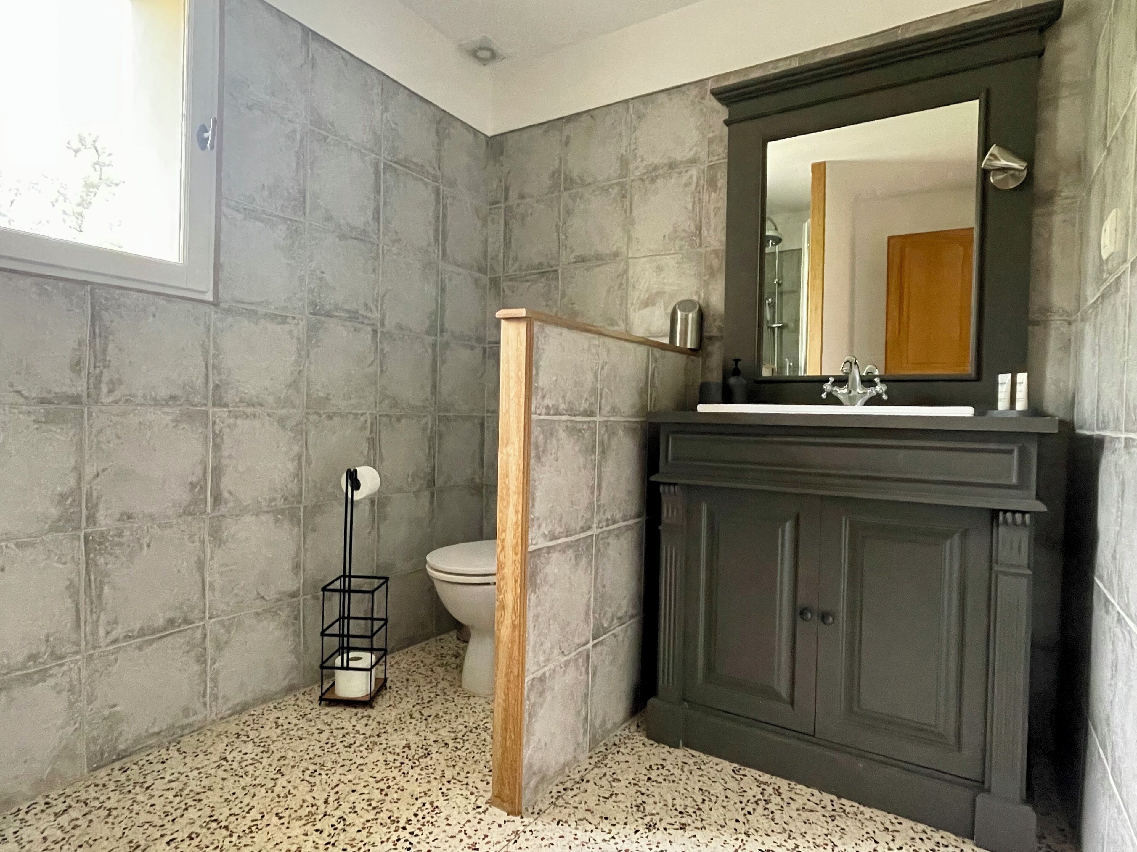 Un baño con inodoro, ducha y lavabo con un mueble oscuro.