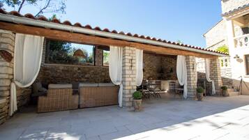 Un área de estar al aire libre con techo, paredes de piedra, muebles de mimbre y plantas en macetas.
