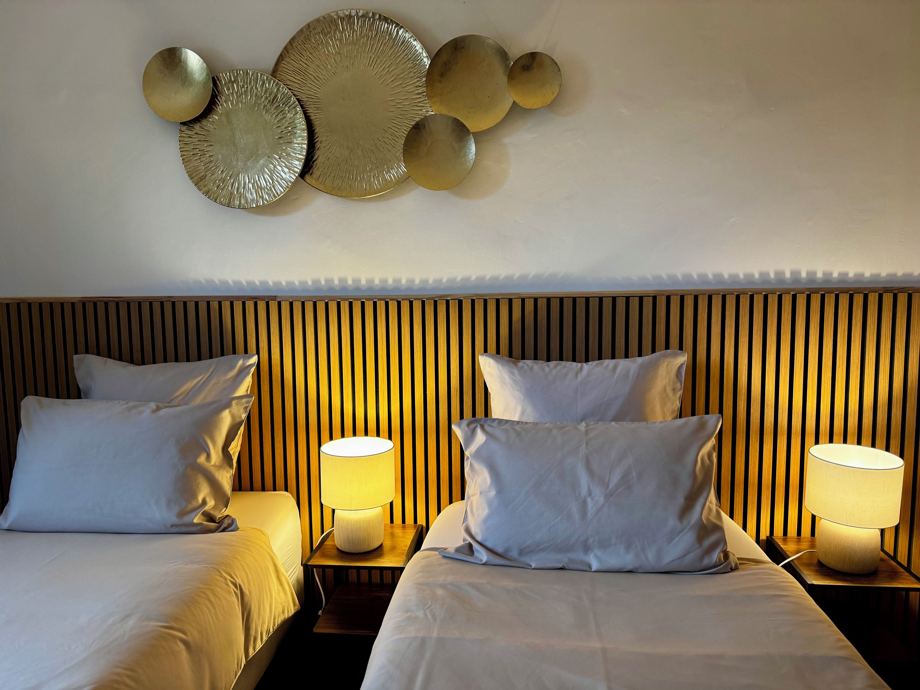 A hotel room with two beds, each with a pillow and a bedside lamp.