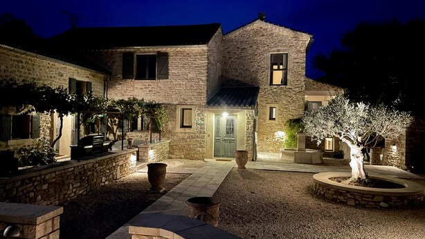 Una casa de piedra con una entrada bien iluminada, un pequeño patio y un jardín con un árbol.