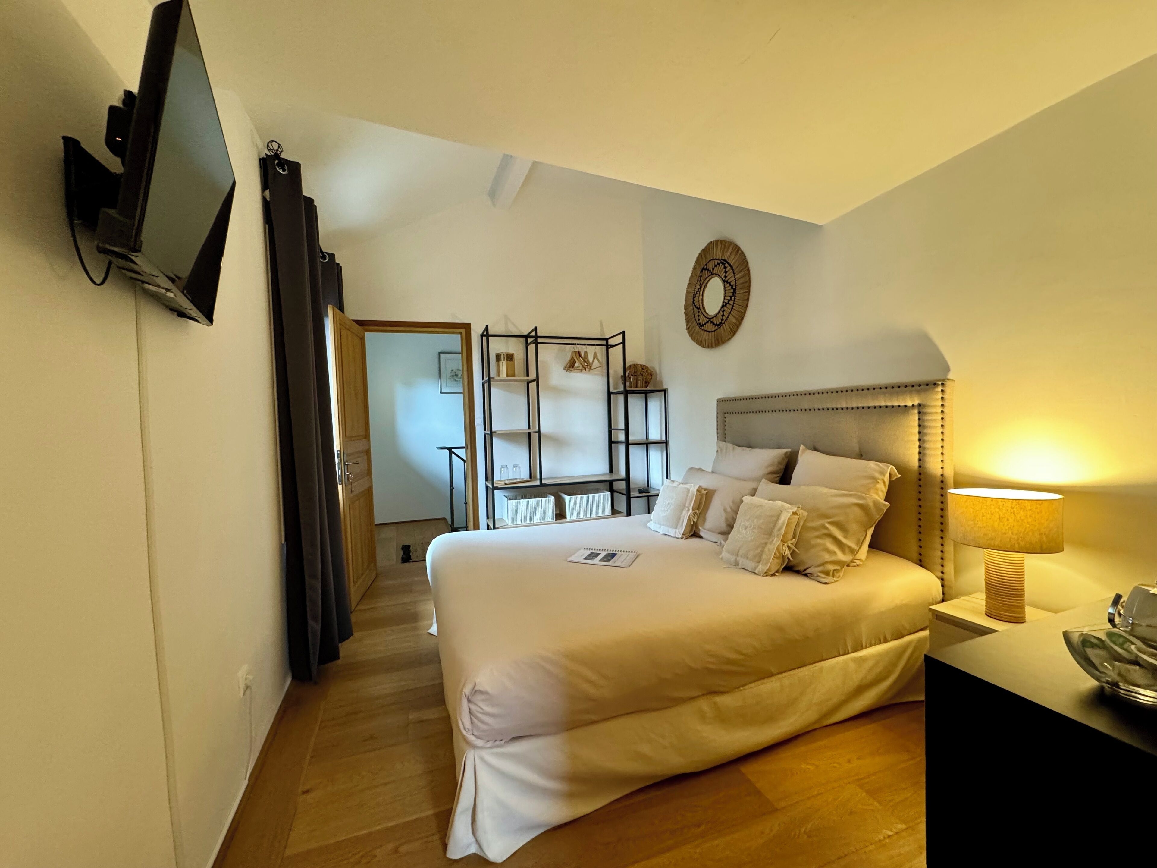 Une chambre avec un grand lit, une table de chevet avec une lampe, un téléviseur fixé au mur et une décoration murale.