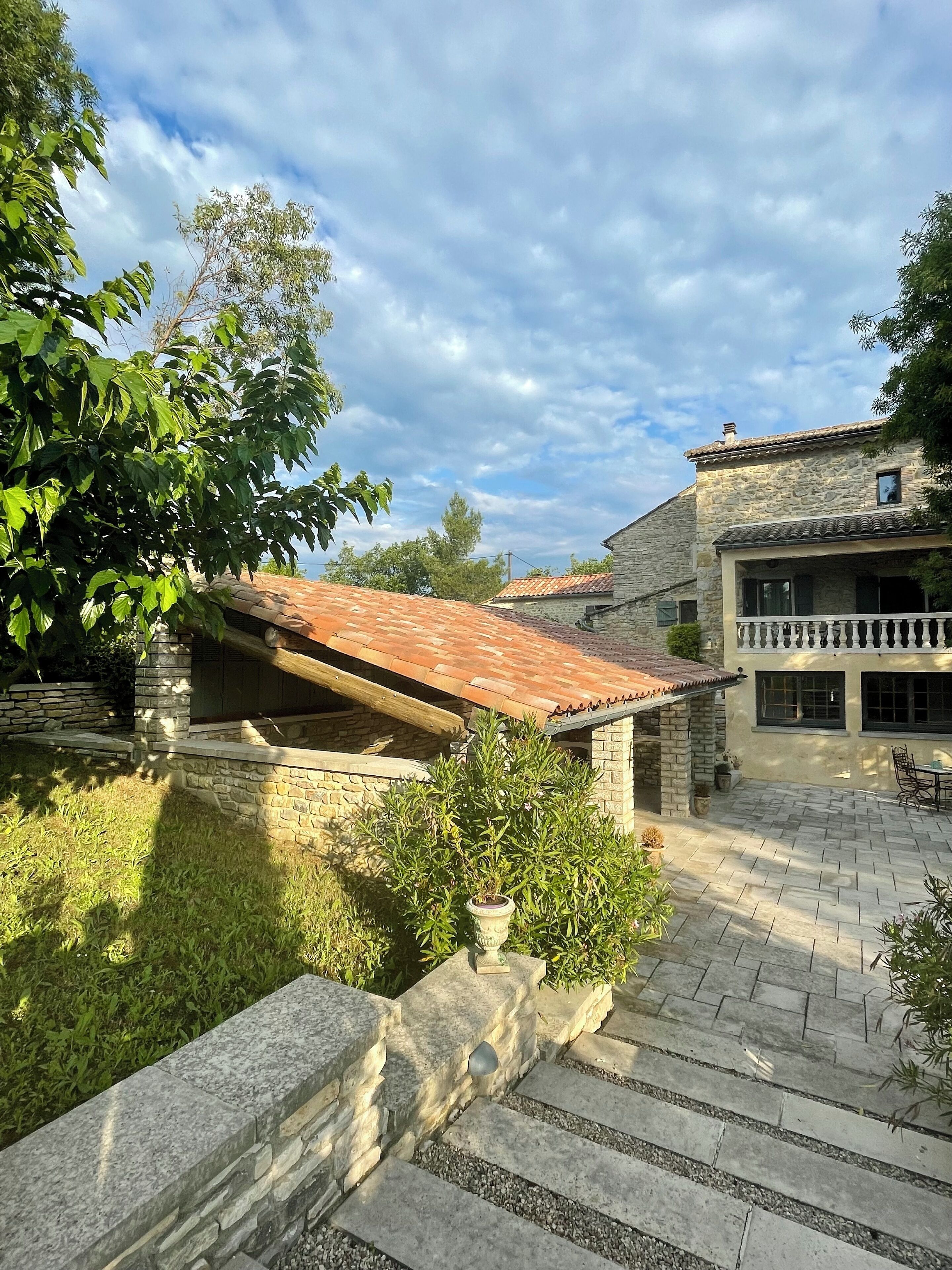 A stone building with a tiled roof, a stone staircase, and a grassy area with a potted plant.