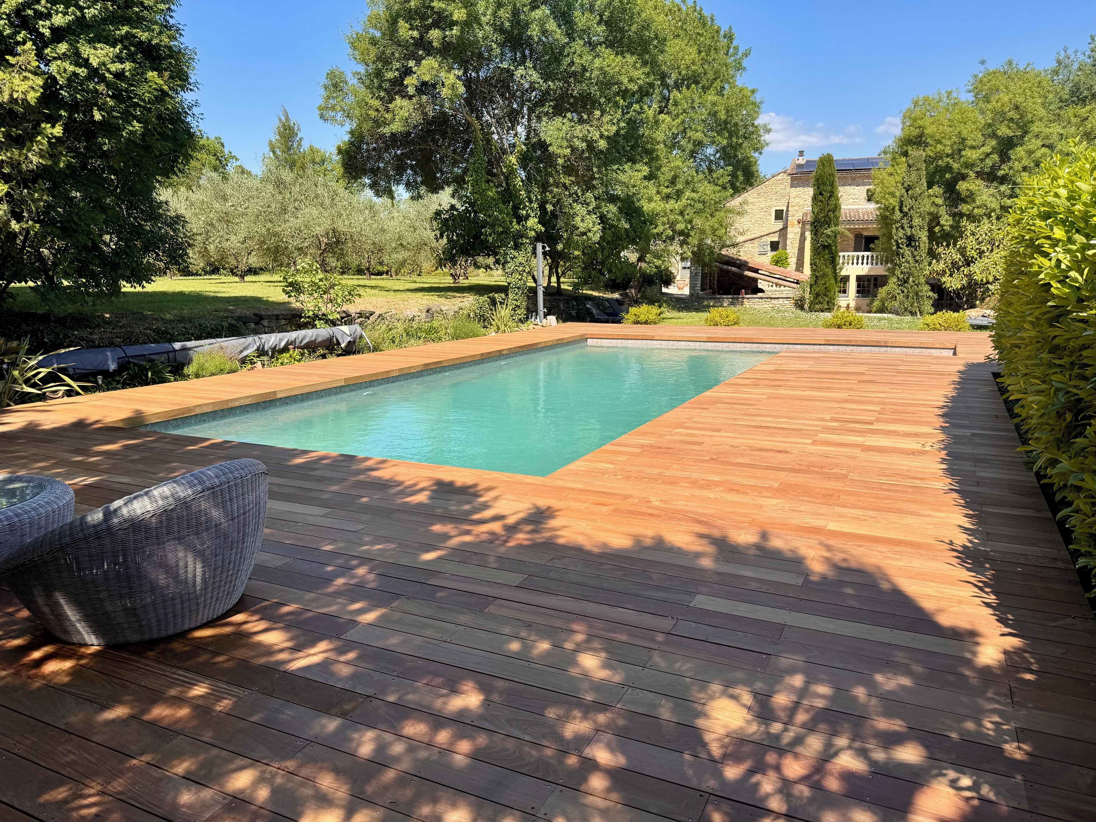 Una piscina rettangolare con un solarium in legno e una sedia in vimini.