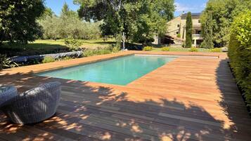 Una piscina rettangolare con un solarium in legno e una sedia in vimini.