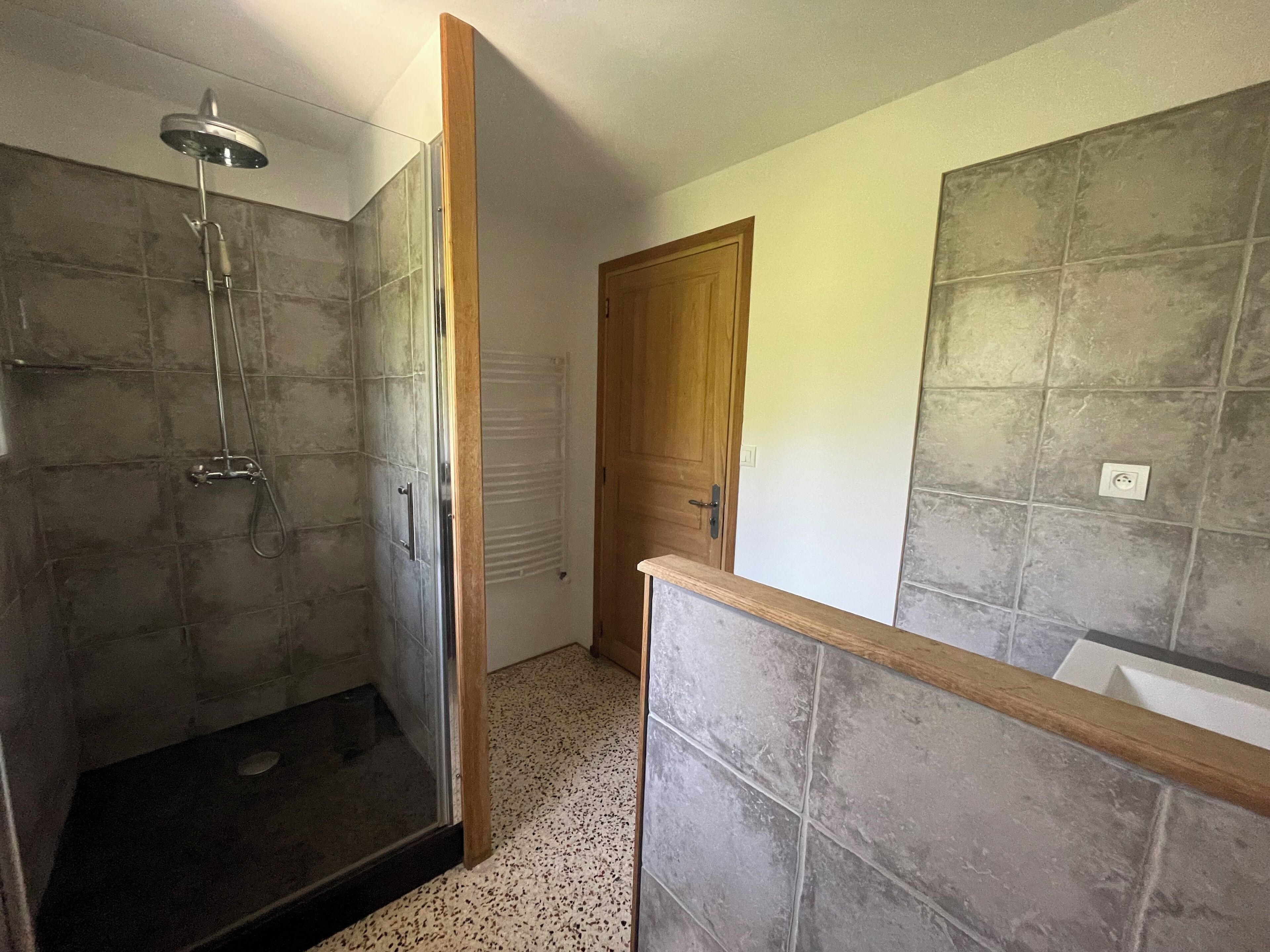 A bathroom with a glass shower enclosure, a wooden door, and tiled walls.
