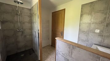 A bathroom with a glass shower enclosure, a wooden door, and tiled walls.