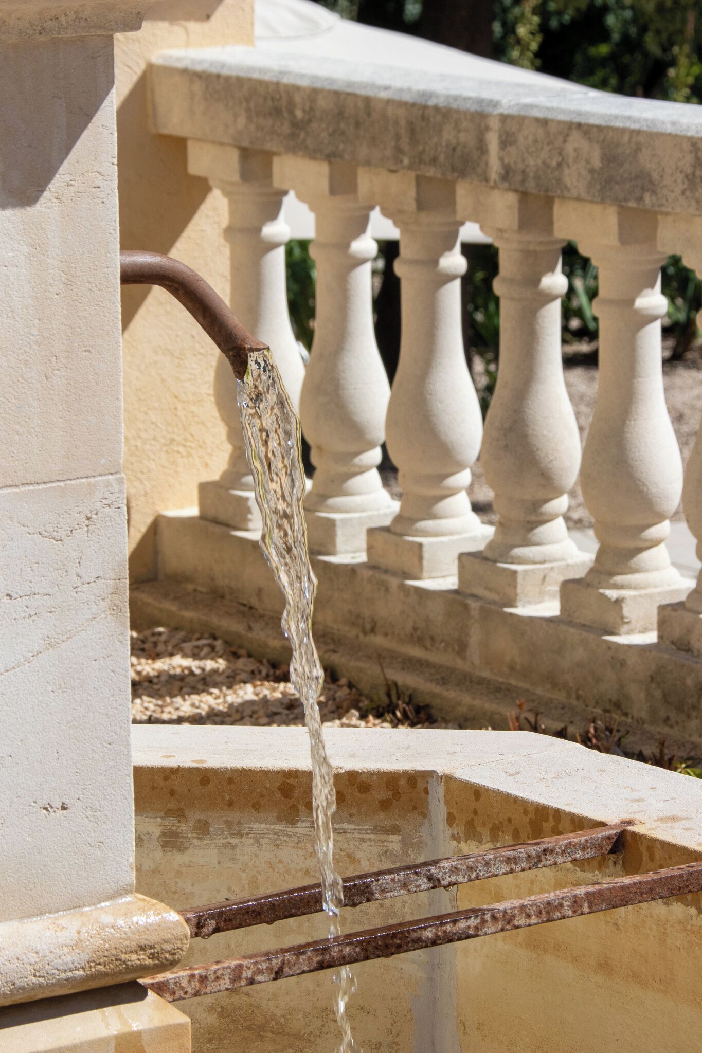 A fountain with water flowing from a rusted metal spout into a rectangular basin.
