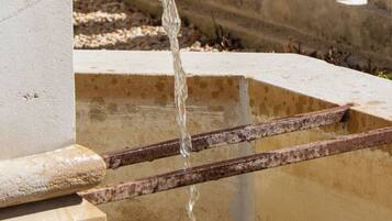 A fountain with water flowing from a rusted metal spout into a rectangular basin.