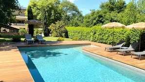 Una piscina rectangular con cubierta de madera y sillas de descanso.