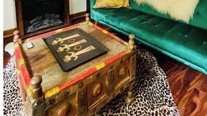 Uma sala de estar com um sofá verde, um espelho decorativo, uma lareira e um tapete estampado.