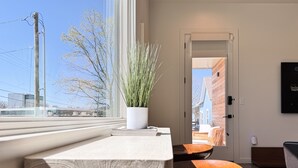 Ein modernes Interieur mit einer Sitzbank an einem Fenster mit Blick auf eine Stadtlandschaft, einer Topfpflanze und einer Tür zu einem Außenbereich.
