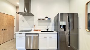 Eine kompakte Küche mit weißen Schränken, einem Edelstahl-Geschirrspüler, einem Kühlschrank mit zwei Türen und einem eingebauten Backofen.