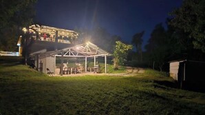 A covered outdoor area with a table and chairs, surrounded by a grassy field and trees. - LAKE HOUSE- Adames Lake House (San Sebastián)