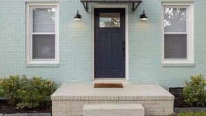 Une maison en briques bleu clair, avec une porte bleu foncé, deux fenêtres de chaque côté et un petit porche avec des marches.
