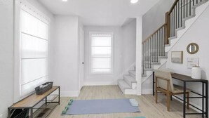 Une pièce spacieuse avec un plancher en bois, un escalier, un bureau et des tapis de sol pour faire de l’exercice.