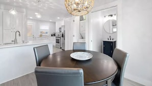 Une cuisine moderne avec des meubles blancs, une table de salle à manger ronde entourée de chaises et un luminaire suspendu au design géométrique original.