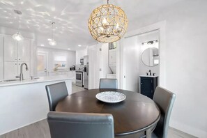 Una cucina moderna con mobili bianchi, un tavolo da pranzo rotondo con sedie e una lampada a sospensione geometrica originale.