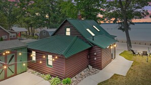 A rustic cabin with a green roof, a small porch, and string lights. - Lakefront Log Cabin-Stunning Lake Views, Kayaks, Steps to Beach & dt Lake City! (Lake City)