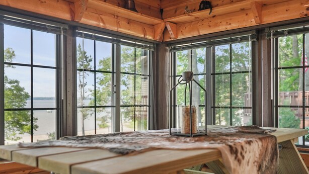 A wooden cabin with large windows, a wooden table, and a hanging light fixture. - Lakefront Log Cabin-Stunning Lake Views, Kayaks, Steps to Beach & dt Lake City! (Lake City)