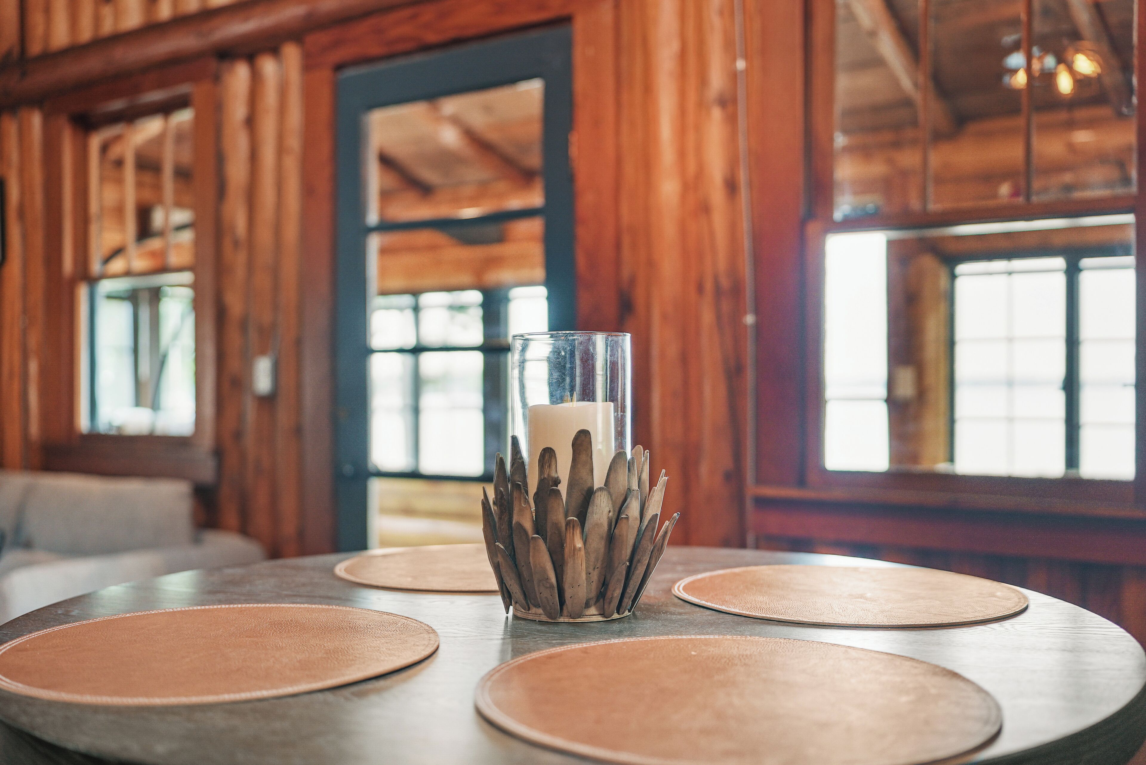 A wooden interior with round tables and a candle in a glass holder.