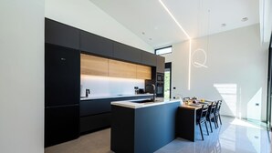 A modern kitchen with dark cabinetry, a central island, and a dining area with chairs.