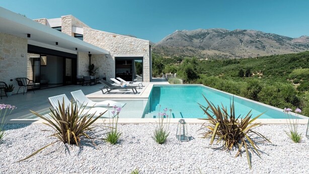 A modern villa with a swimming pool, outdoor seating, and a view of the mountains.