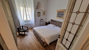 Une chambre à coucher avec un lit, une chaise, une table de chevet et une fenêtre avec des rideaux.