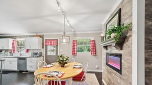 A modern kitchen with white cabinets, a wooden dining table, and red and white checkered curtains. - Greensboro Golf Getaway - 9 Mi to Downtown! (Greensboro)