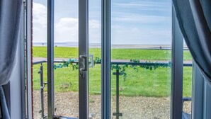 Ein Zimmer mit einer großen Glasdoor, die auf einen Balkon mit Blick auf eine Wiese und ein Gewässer führt.