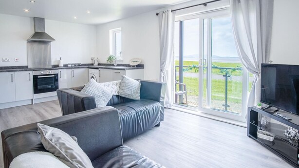 Ein modernes Wohnzimmer mit grauem Sofa, einem Flachbildfernseher und einer Glastür, die auf einen Balkon führt.