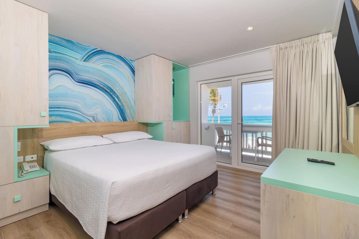Une chambre d’hôtel avec un grand lit, un bureau, une télévision et un balcon donnant sur l’océan.