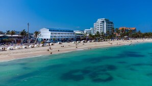 Un hôtel en bord de mer composé de plusieurs bâtiments, doté d’une plage de sable et bordé de palmiers.