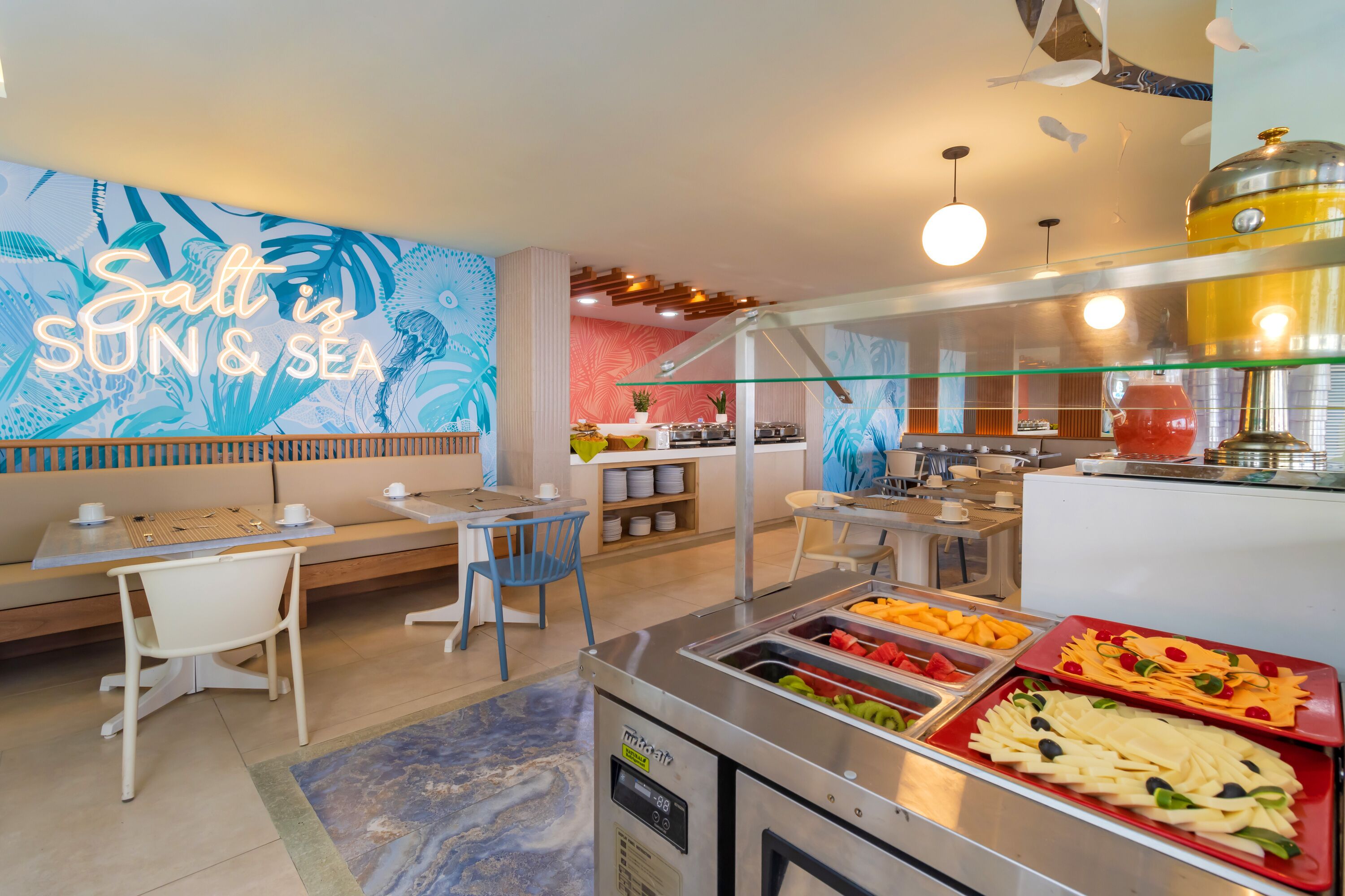 A buffet area with a variety of food options, a seating area with a mural, and a modern kitchen in the background.