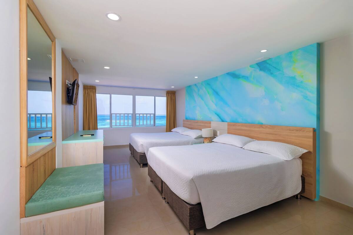 Une chambre d’hôtel avec deux lits, une grande fenêtre donnant sur la mer et un tableau accroché au mur.