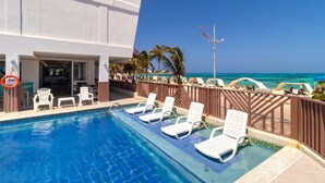 Un espace piscine avec des chaises longues blanches, une bouée de sauvetage et une vue sur l’océan.