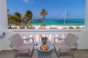 Un balcon avec deux chaises, une table sur laquelle se trouve une assiette de fruits et une bouteille de champagne, et une vue sur la plage et l’océan.