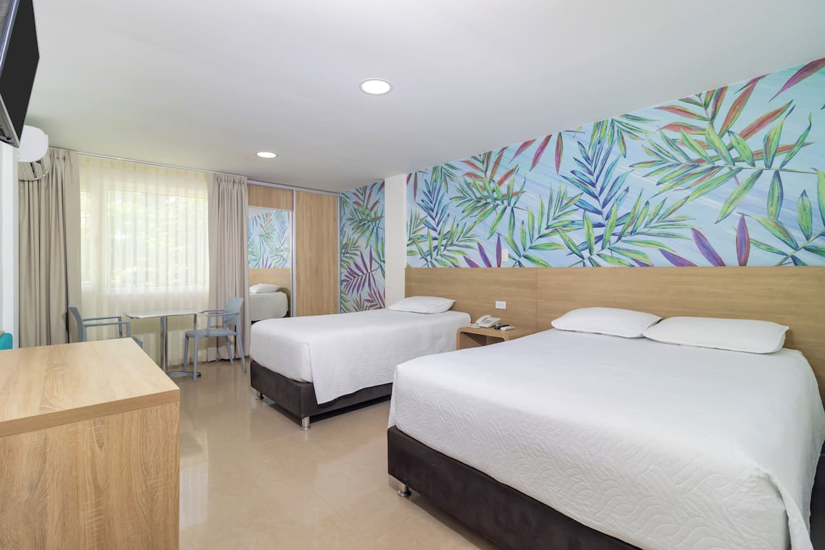 Une chambre d’hôtel avec deux lits, un bureau, une chaise, une petite table et un mur orné d’un motif de feuilles tropicales.