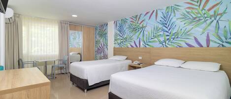 A hotel room with two beds, a desk, a chair, a small table, and a wall with a tropical leaf pattern.