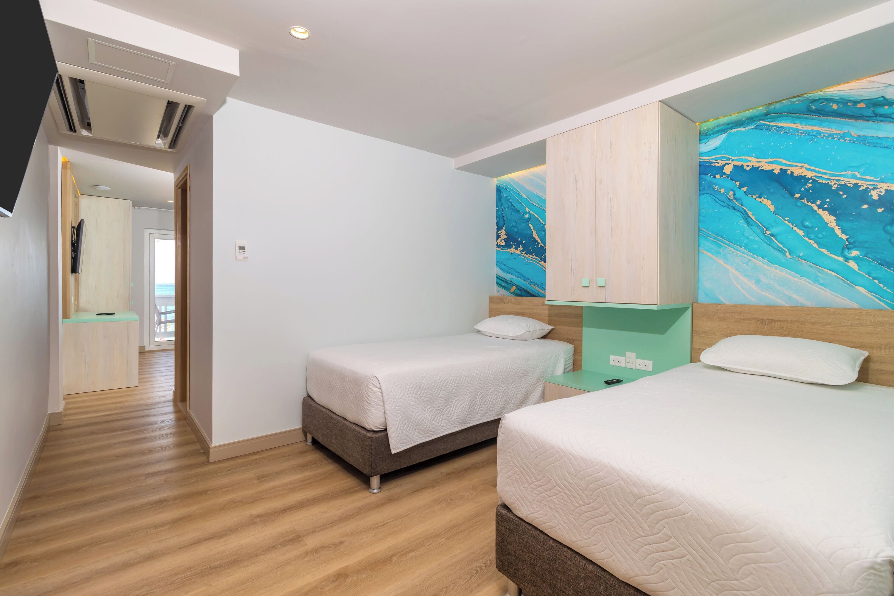 A hotel room with two beds, wooden flooring, a large abstract painting on the wall, and a wooden wardrobe.