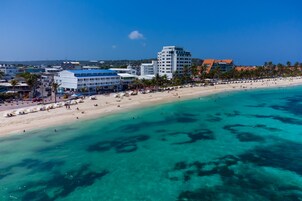 Un hotel frente al mar con vista a la playa, varios pisos y una mezcla de arquitectura moderna y tradicional.