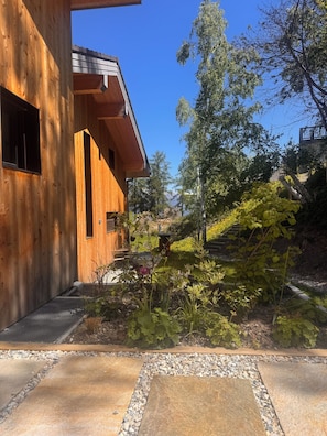 Un bâtiment en bois doté d’un toit en pente, d’un chemin en pierre et entouré de verdure.