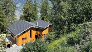 Una baita di legno con tetto spiovente, immersa in una fitta foresta con montagne sullo sfondo.