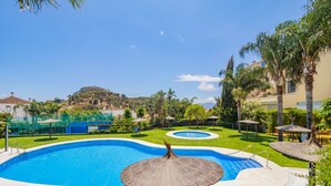 Une piscine avec un jacuzzi circulaire, entourée d’une pelouse bien entretenue et de palmiers.