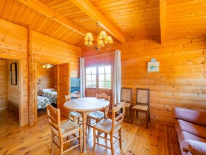 Cozy cabin interior with a round dining table, sofa, and TV, set amidst high ceilings and large windows.