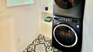 Une buanderie équipée d’un lave-linge et d’un sèche-linge à chargement frontal, d’une fenêtre donnant sur un espace verdoyant et d’un sol à motifs.