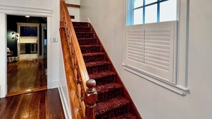 Un escalier avec des rampes en bois et une moquette à motifs, menant à une pièce ornée d’un lustre.