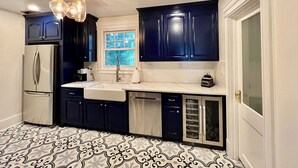 Une cuisine moderne avec des meubles de couleur bleu foncé, un réfrigérateur blanc, un évier et une fenêtre donnant sur des arbres.