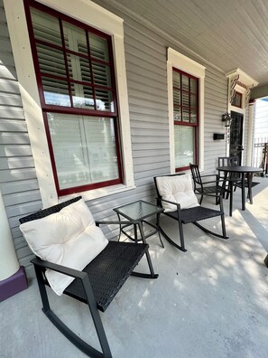 A covered porch with two rocking chairs and a small table, white walls, and large windows with red frames. - Downtown Macon Cottage Walking Distance to Dining & Music Venues. 2 King Beds. (Macon)