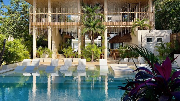 Un resort con piscina, sillas de descanso y un espacio al aire libre techado con estructuras de bambú.